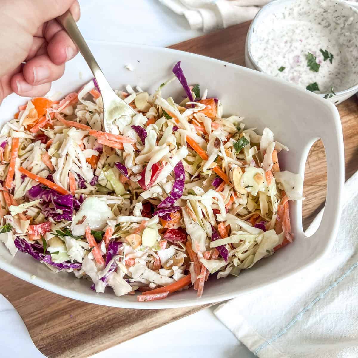 bowl of coleslaw with hand holding a gold fork in the bowl