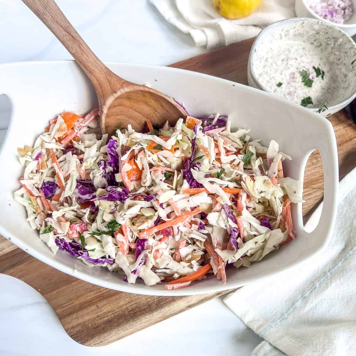 bowl of coleslaw with spoon in it and a small bowl of dressing to the side