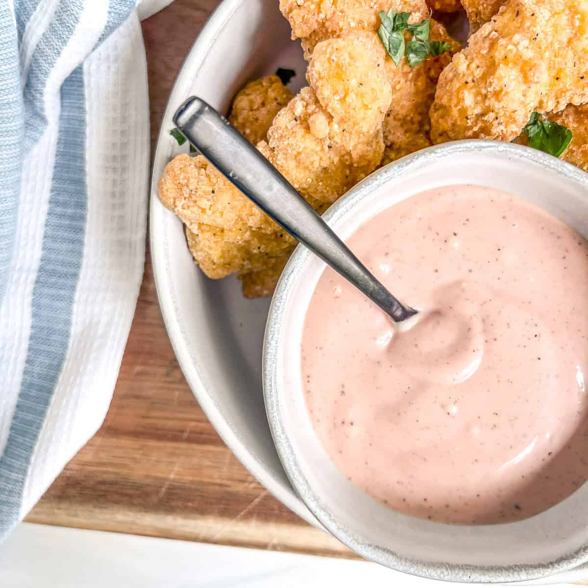 close up pic of chicken dipping sauce and chicken tenders around the sauce