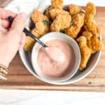hand holding a spoon of chicken sauce and chicken tenders above the sauce