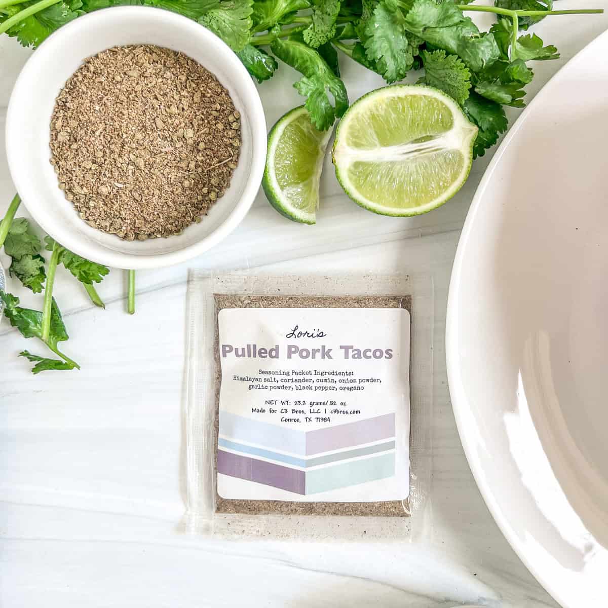 pulled pork seasoning packet with fresh cilantro and fresh limes above it and a bowl of seasonings above the packet