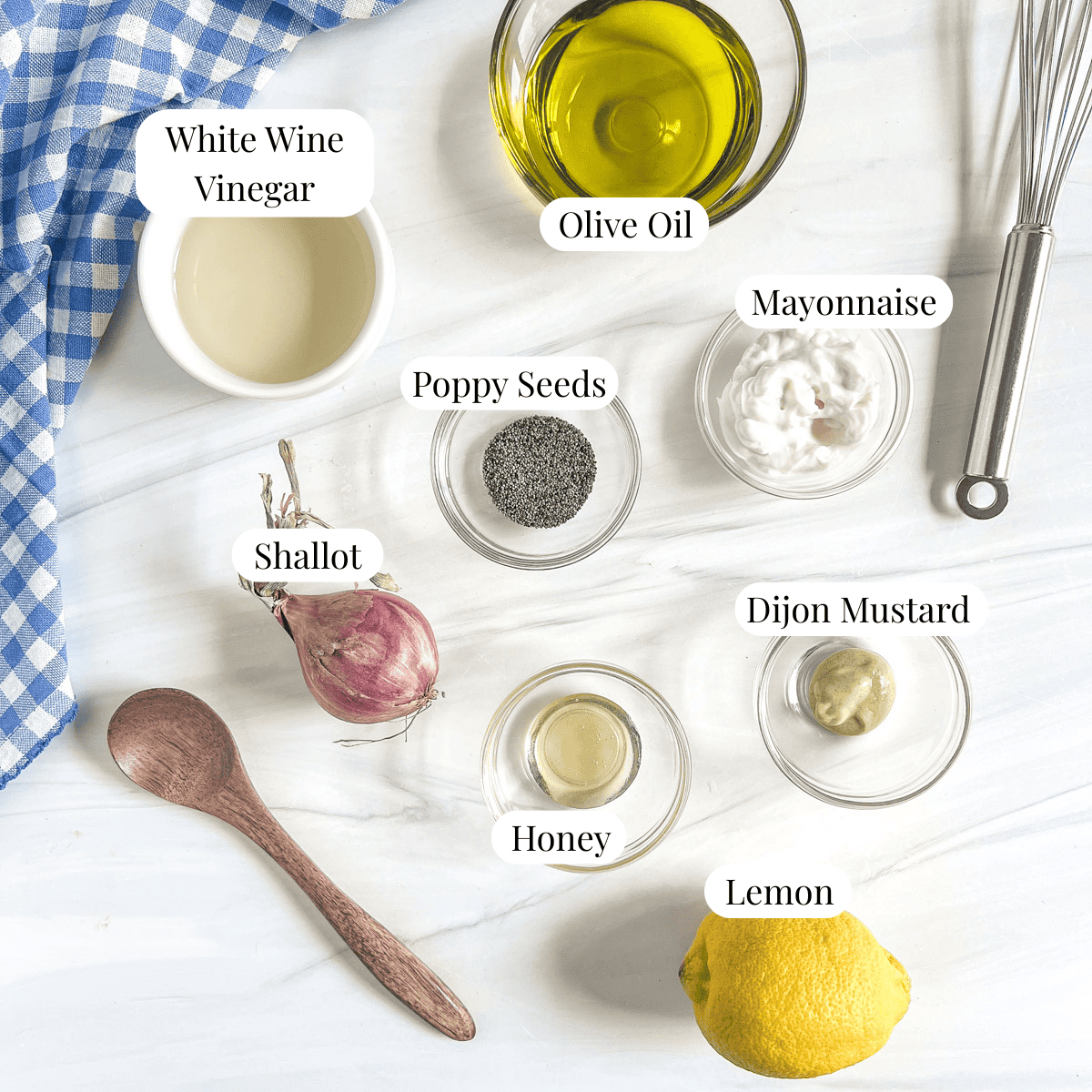 whole lemon, bowl with honey, bowl with dijon mustard, shallot, bowl of poppy seeds, bowl of mayonnaise, bowl of olive oil, bowl of white wine vinegar and a whisk and wooden spoon to the side