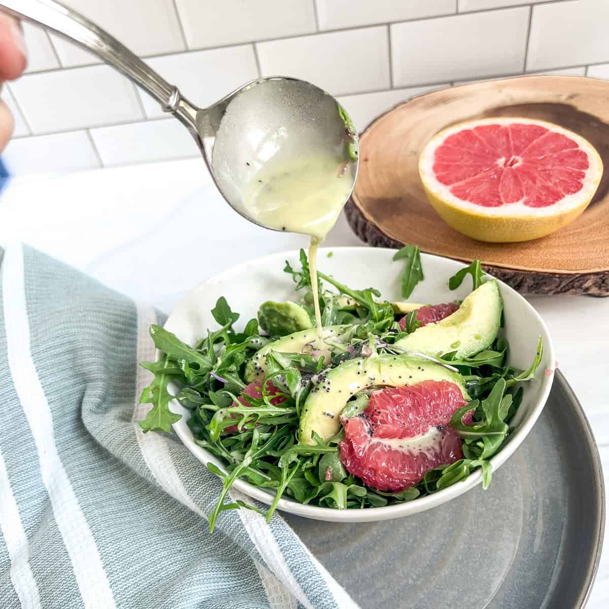 bowl of avocado and grapefruit slivers on lettuce and a spoon pouring dressing over the salad