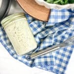jar of poppy seed salad dressing on a blue and white napkin and a whisk