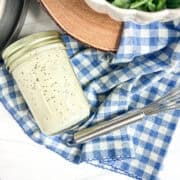 jar of poppy seed salad dressing on a blue and white napkin and a whisk