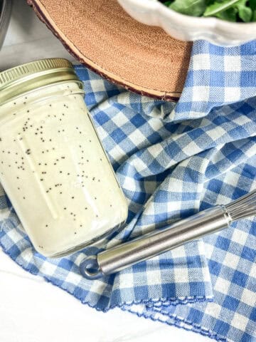 jar of poppy seed salad dressing on a blue and white napkin and a whisk