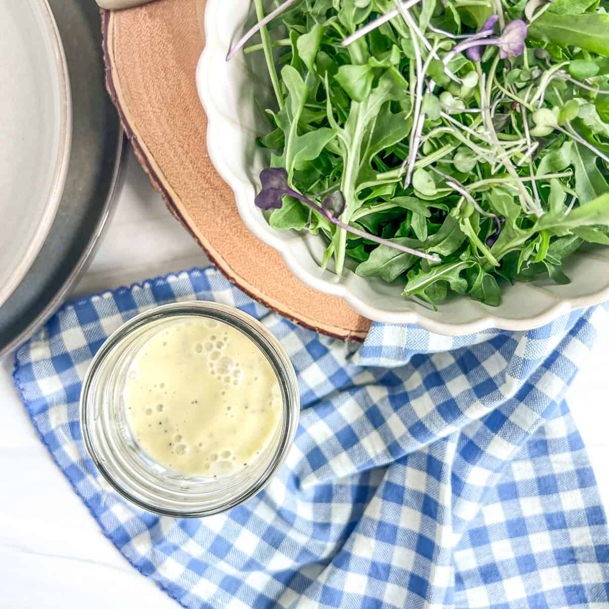 jar of salad dressing with a bowl of lettuce on a blue and white napkin
