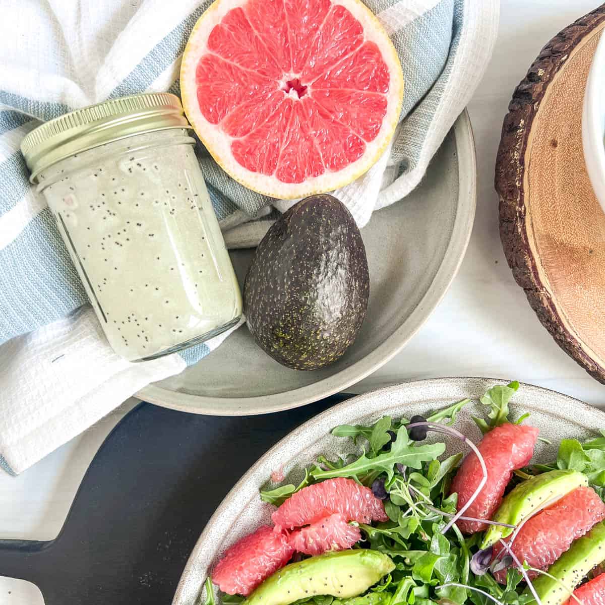 jar of salad dressing with an avocado and half of a grapefruit in a bowl and a blue and white napkin underneath