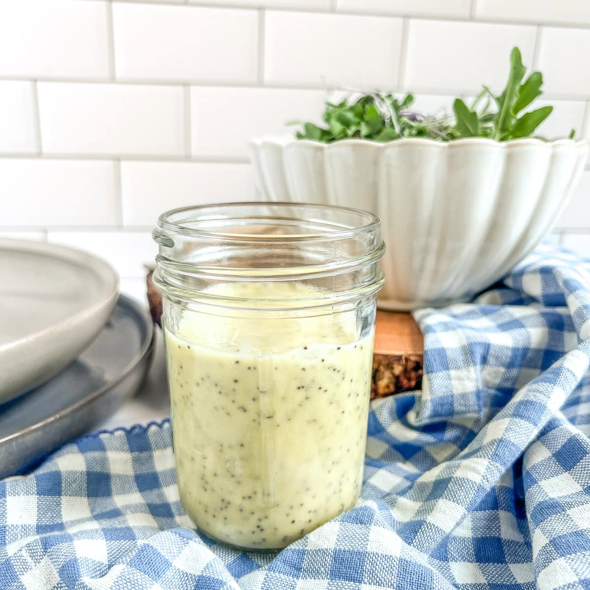 jar or salad dressing and a bowl of salad on a blue and white napkin