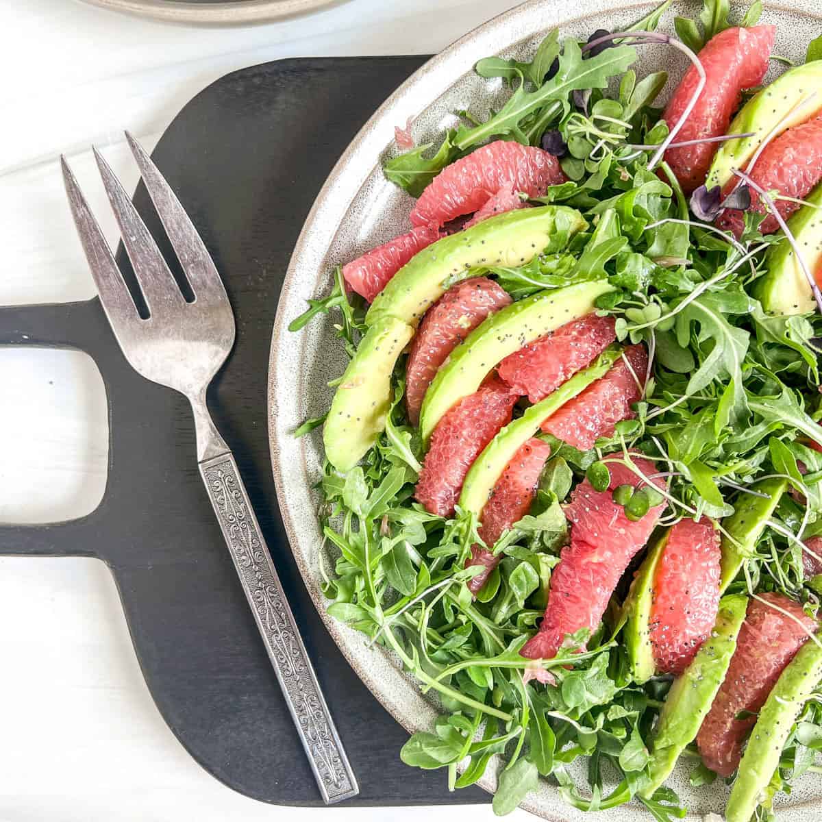 plate of grapefruit and avocado slices with lettuce and a large serving fork to the side