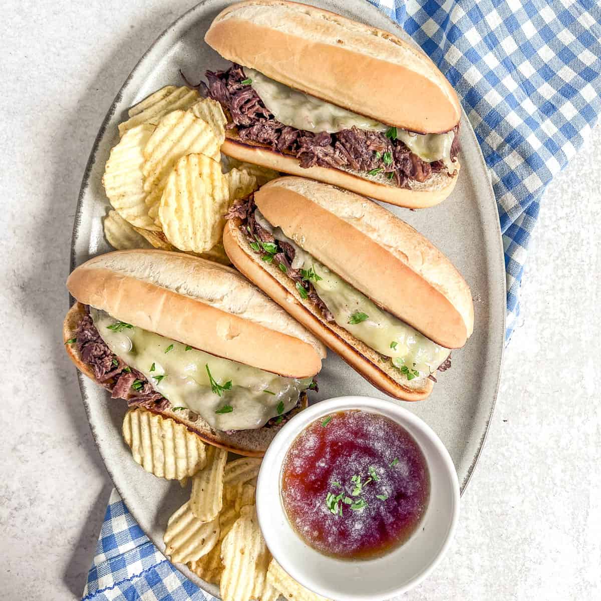 Slow Cooker Pot roast french dip sandwiches on a platter with chips