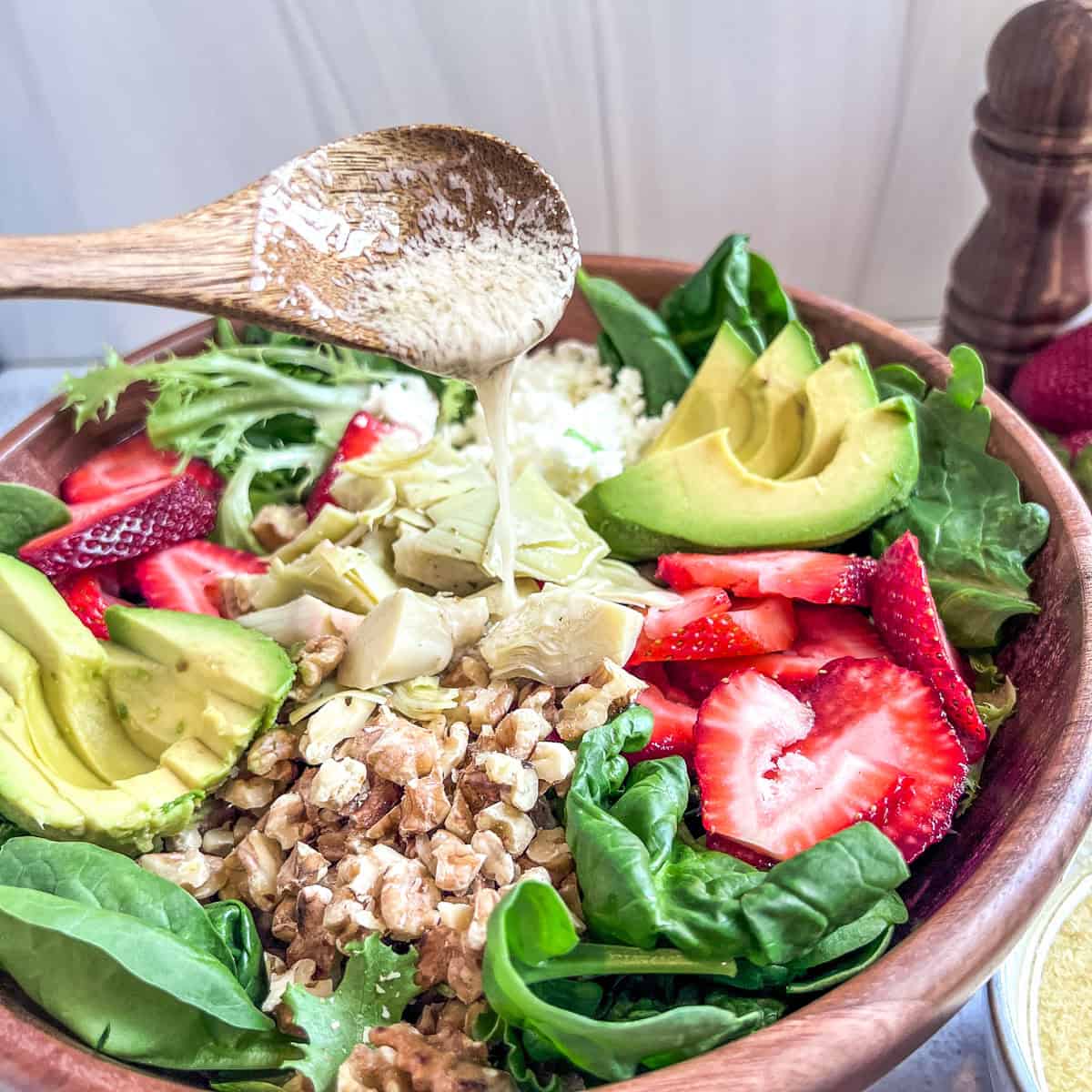 Strawberry Walnut Salad ingredients in a bowl spoon pouring dressing