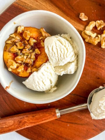 baked peaches in white bowl with ice cream