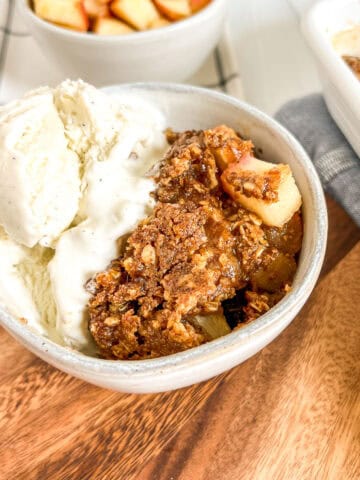baked apple dessert with ice cream in a white bowl