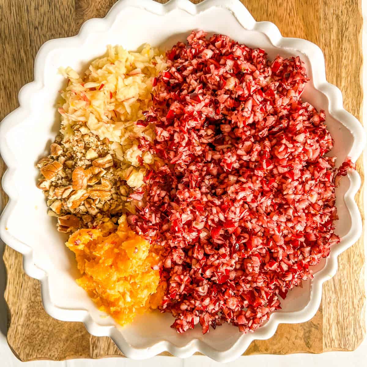 chopped cranberries, apples, oranges with chopped nuts in white bowl