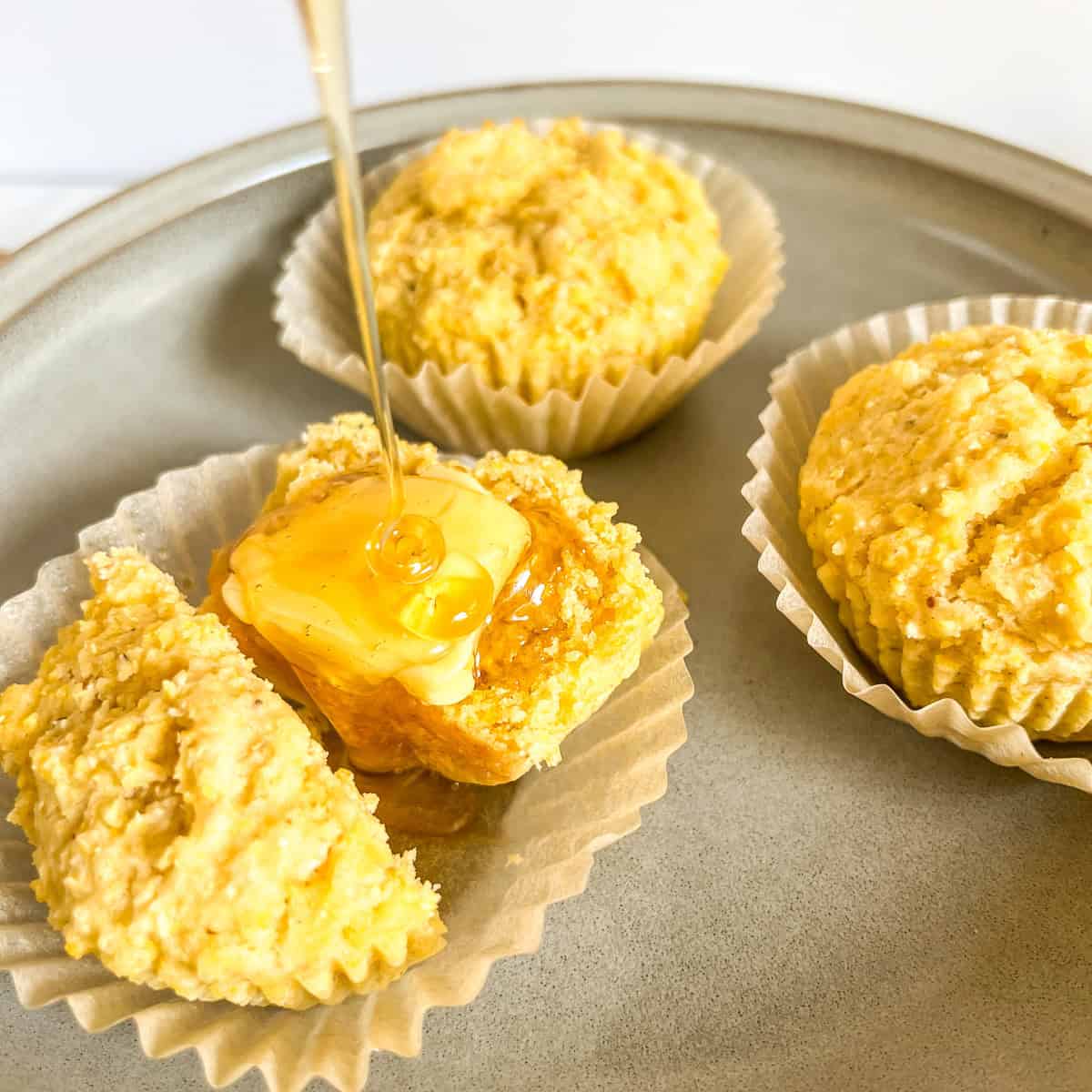close up of cornbread muffin cut in half with butter and honey
