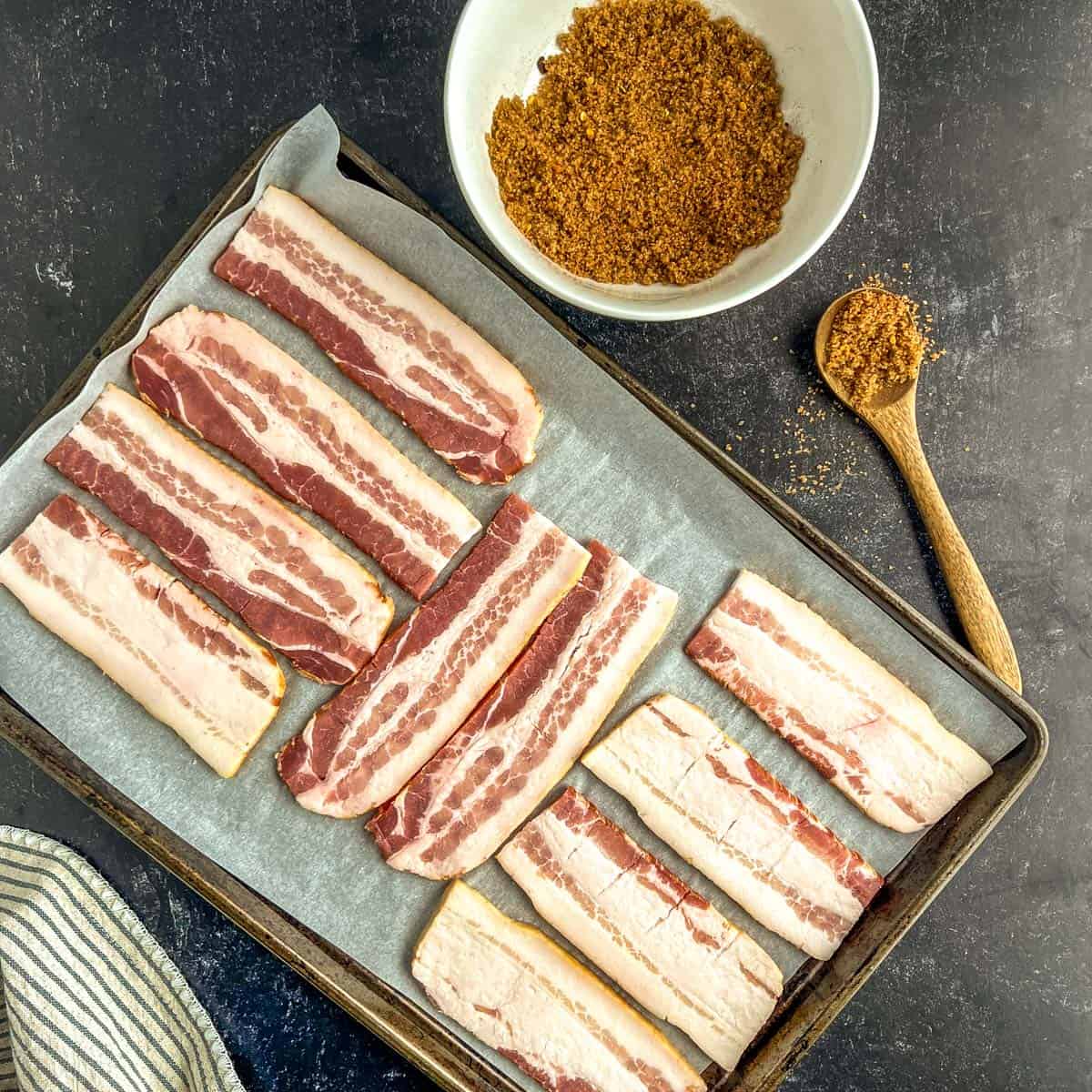 pieces of bacon on a baking sheet with a bowl of brown sugar