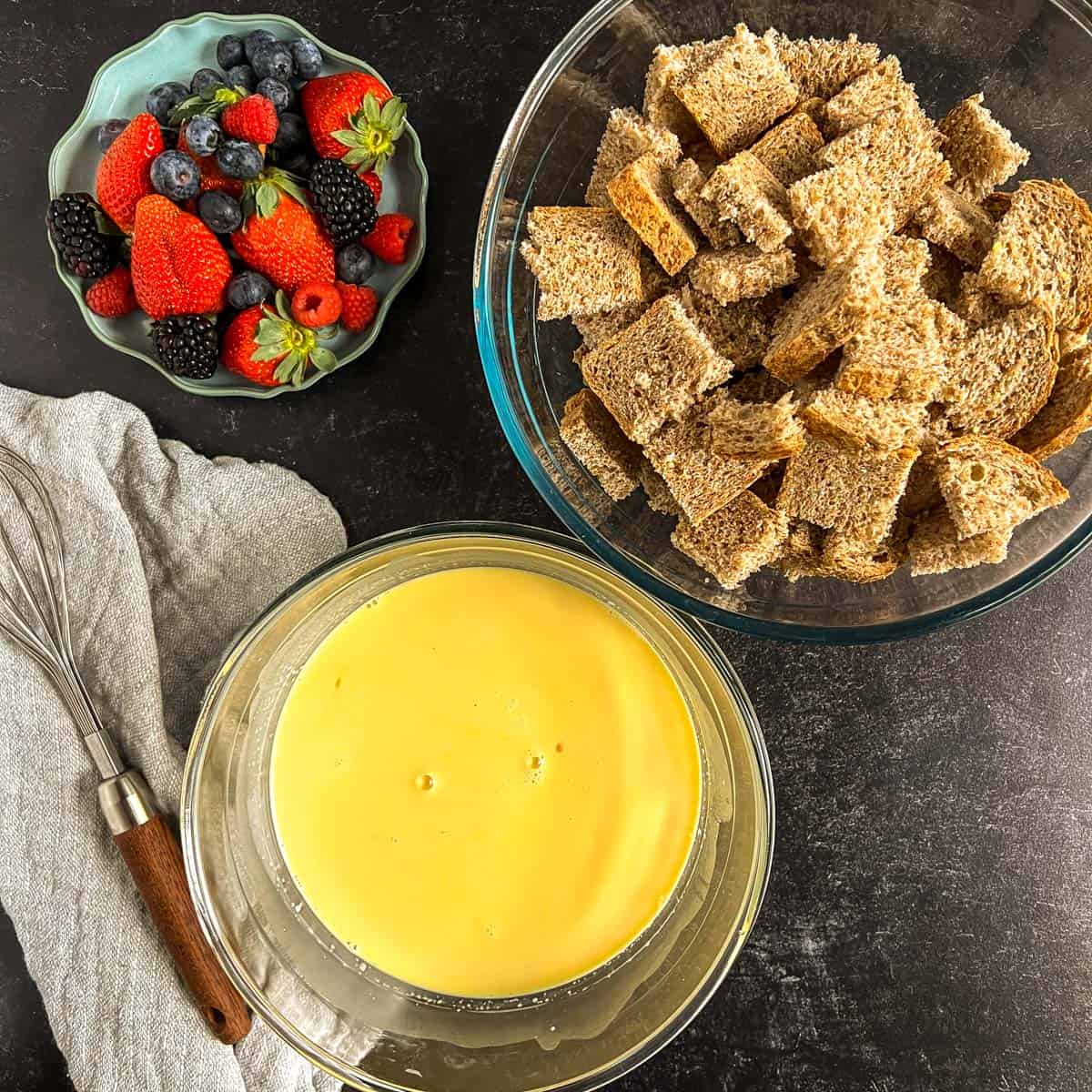 pieces of bread in a bowl, custard in a bowl, berries to the side